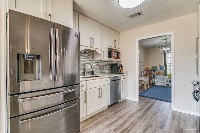 kitchen featuring white cabinets, sink, a textured ceiling, light hardwood / wood-style flooring, and appliances with stainless steel finishes