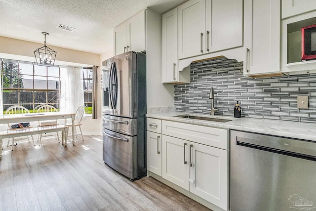 kitchen with light wood-type flooring, light stone counters, white cabinets, sink, and appliances with stainless steel finishes