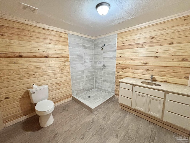 full bath featuring visible vents, wood walls, a shower stall, a textured ceiling, and wood finished floors