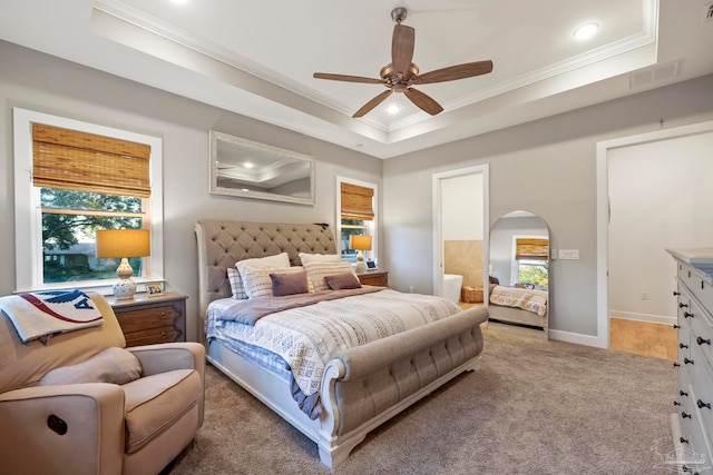 carpeted bedroom with ceiling fan, ornamental molding, a tray ceiling, and multiple windows