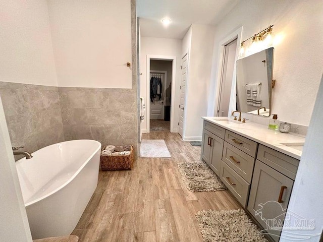 bathroom with hardwood / wood-style floors, vanity, a bath, and tile walls