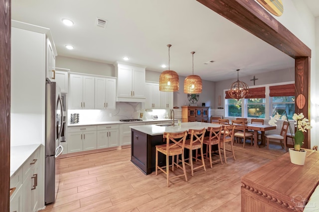 kitchen with pendant lighting, white cabinetry, an island with sink, and light hardwood / wood-style flooring