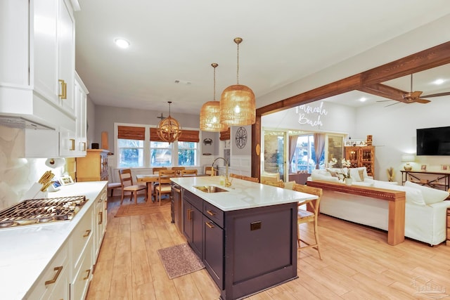 kitchen featuring decorative light fixtures, stainless steel gas stovetop, white cabinets, ceiling fan with notable chandelier, and light wood-type flooring