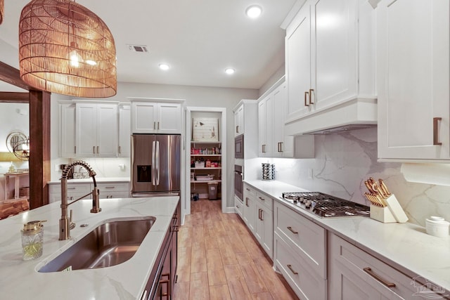 kitchen with sink, stainless steel appliances, light hardwood / wood-style flooring, decorative light fixtures, and white cabinets