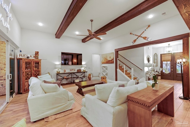 living room featuring french doors, ceiling fan with notable chandelier, beam ceiling, light hardwood / wood-style flooring, and a high ceiling