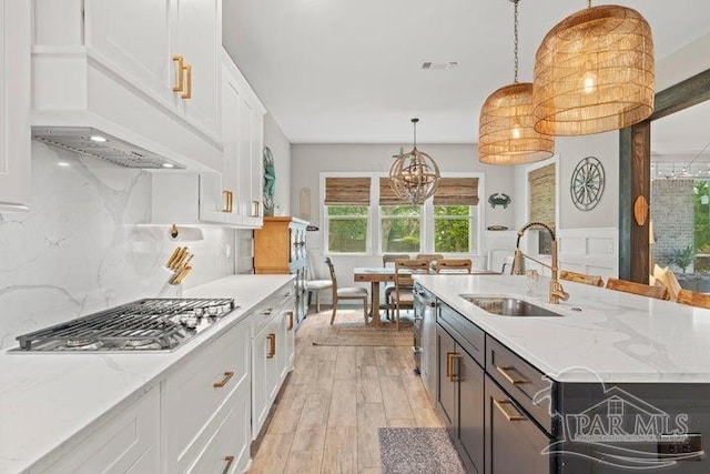 kitchen with white cabinets, sink, hanging light fixtures, light wood-type flooring, and an island with sink