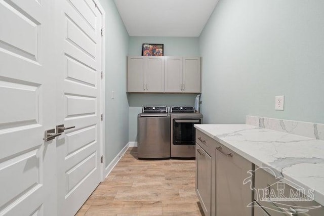 clothes washing area with washer and dryer, cabinets, and light wood-type flooring