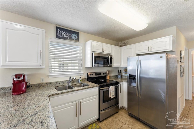 kitchen with stainless steel appliances, light stone counters, white cabinets, a textured ceiling, and sink