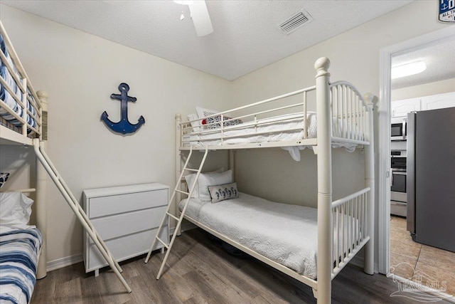 bedroom featuring dark wood-type flooring, stainless steel fridge, a textured ceiling, and ceiling fan