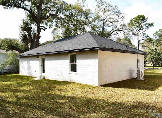 view of side of home with ac unit, a yard, brick siding, and a shingled roof