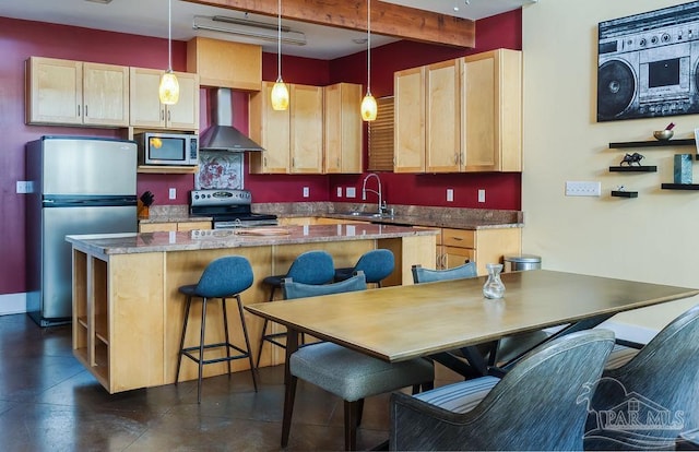 kitchen with pendant lighting, wall chimney exhaust hood, stainless steel appliances, and light brown cabinetry