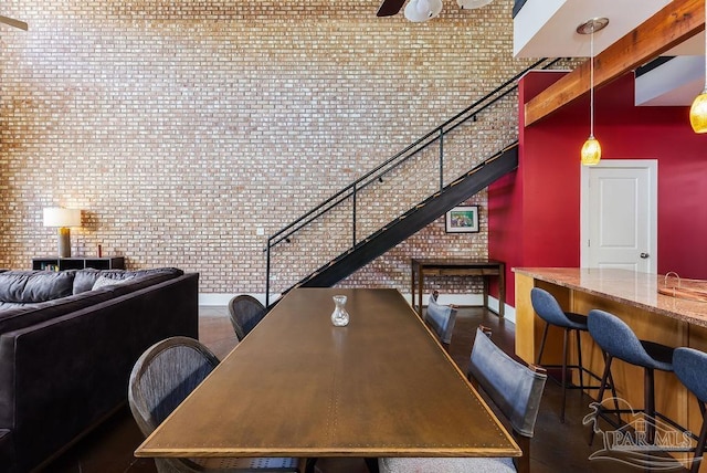 dining area with a towering ceiling, beamed ceiling, and brick wall