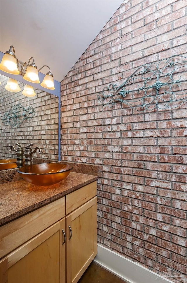 bathroom featuring vanity, brick wall, and lofted ceiling