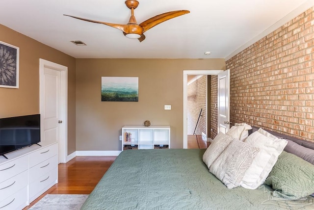 unfurnished bedroom with ceiling fan, brick wall, and wood-type flooring