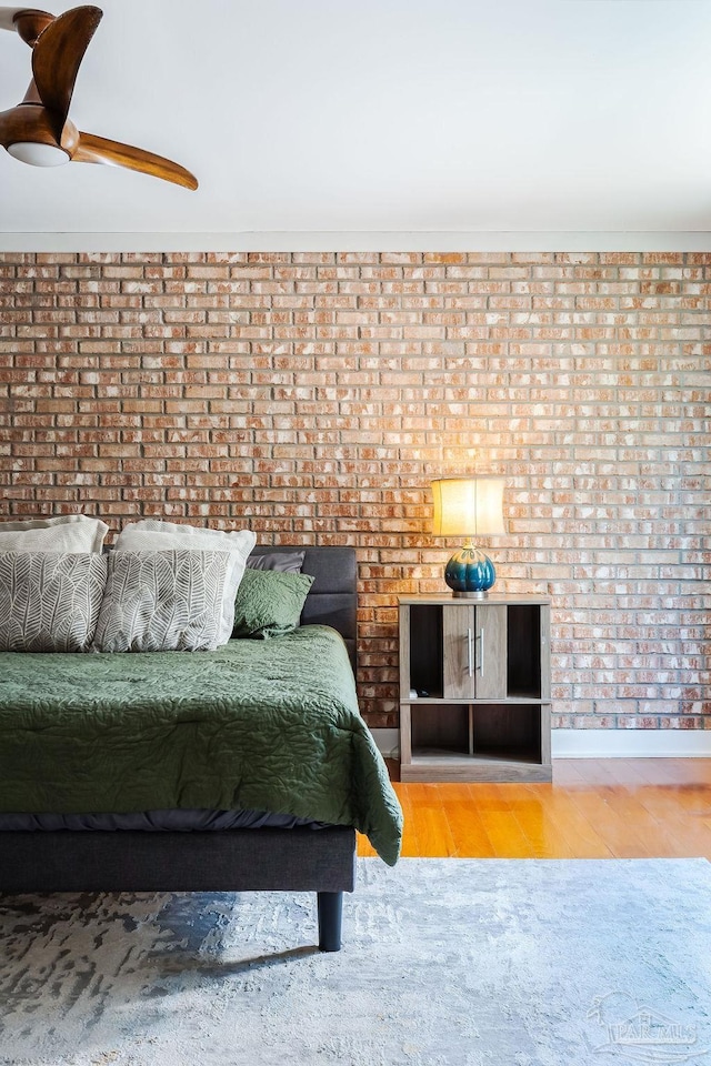 unfurnished bedroom featuring ceiling fan, wood-type flooring, and brick wall