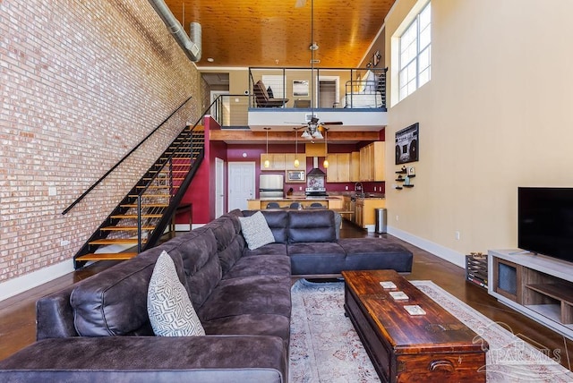 living room with ceiling fan, sink, a high ceiling, and brick wall