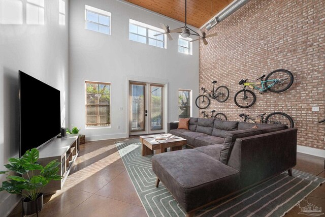 living room featuring ceiling fan, a towering ceiling, wooden ceiling, and brick wall