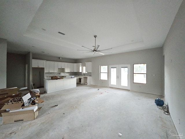 unfurnished living room featuring a tray ceiling, ceiling fan, and french doors