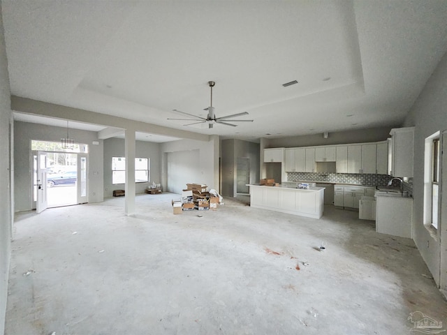 unfurnished living room featuring a tray ceiling, sink, and ceiling fan with notable chandelier