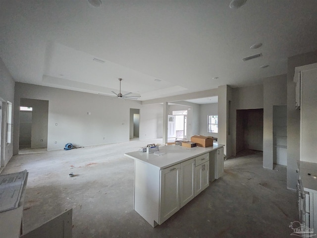 kitchen with white cabinetry, ceiling fan, a tray ceiling, and a kitchen island