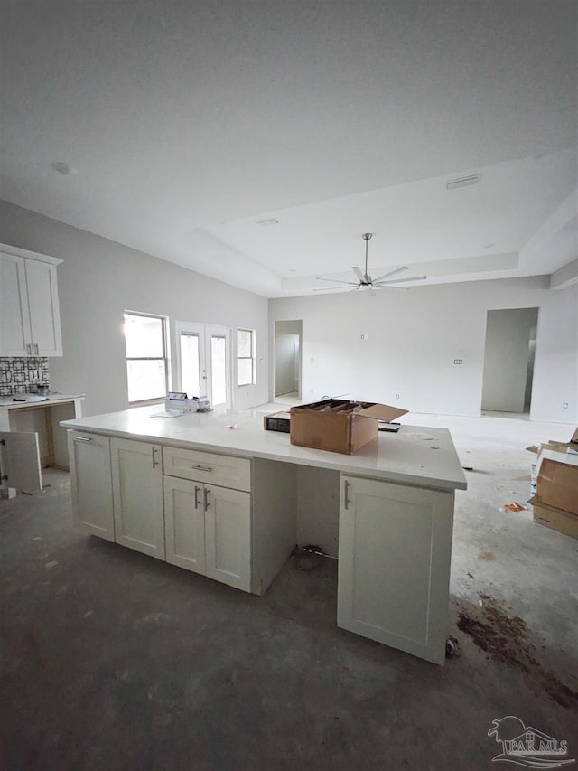 kitchen featuring white cabinets, a tray ceiling, a kitchen island, and ceiling fan