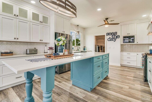 kitchen with stainless steel range with gas stovetop, custom exhaust hood, white cabinetry, backsplash, and light hardwood / wood-style floors