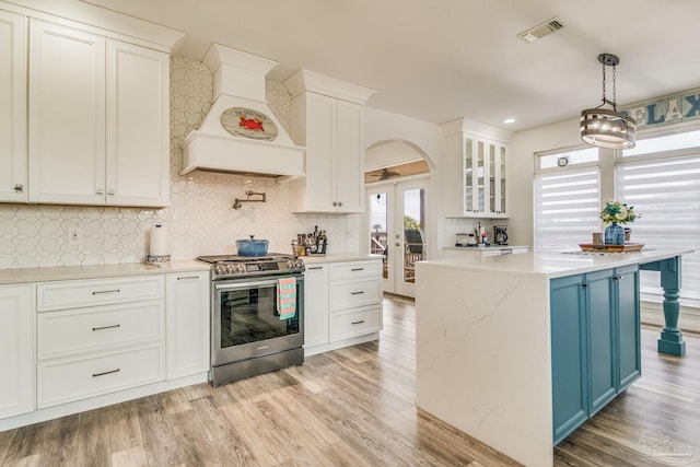 kitchen featuring arched walkways, visible vents, light wood-style floors, premium range hood, and stainless steel gas range oven