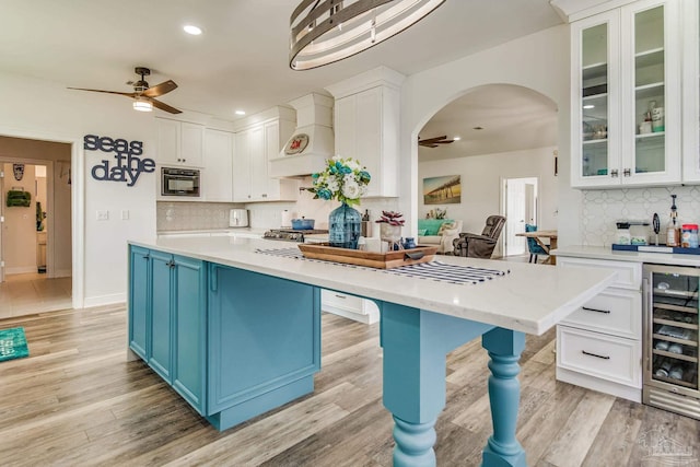 kitchen with white cabinets, light wood-style flooring, custom range hood, wine cooler, and blue cabinets