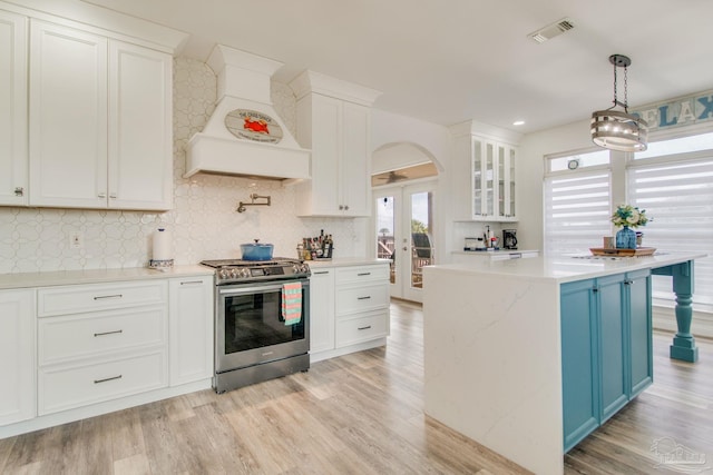 kitchen featuring hanging light fixtures, custom exhaust hood, stainless steel range, and light wood-type flooring