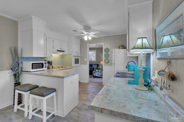 kitchen featuring white appliances, sink, crown molding, kitchen peninsula, and white cabinetry