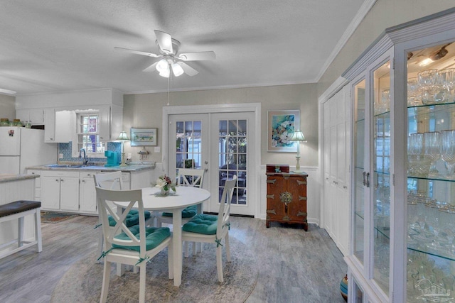 dining area with french doors, a textured ceiling, ceiling fan, crown molding, and light hardwood / wood-style flooring