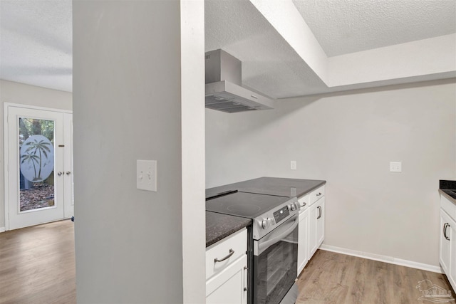 kitchen featuring dark countertops, stainless steel electric range, a textured ceiling, light wood-type flooring, and wall chimney range hood