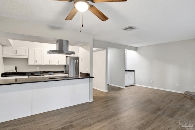 kitchen with dark countertops, visible vents, freestanding refrigerator, a sink, and wall chimney range hood