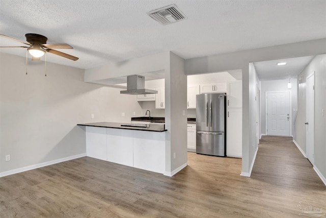 kitchen with wood finished floors, visible vents, white cabinets, ventilation hood, and freestanding refrigerator