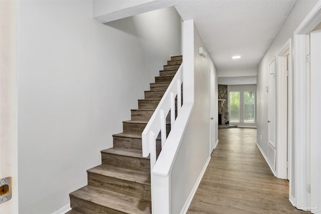 staircase featuring a textured ceiling, baseboards, a fireplace, and wood finished floors