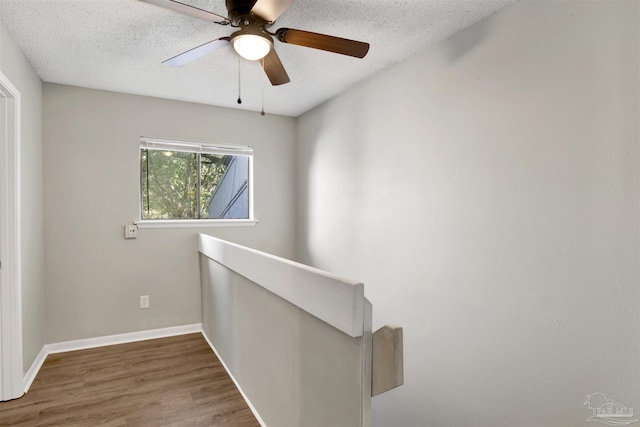 hallway featuring a textured ceiling, baseboards, and wood finished floors