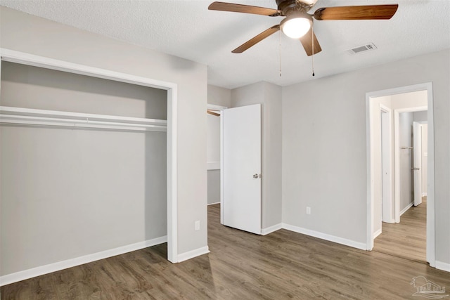 unfurnished bedroom featuring a closet, visible vents, a textured ceiling, wood finished floors, and baseboards