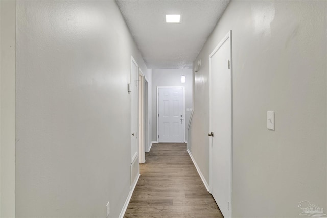 corridor featuring a textured ceiling, baseboards, and wood finished floors