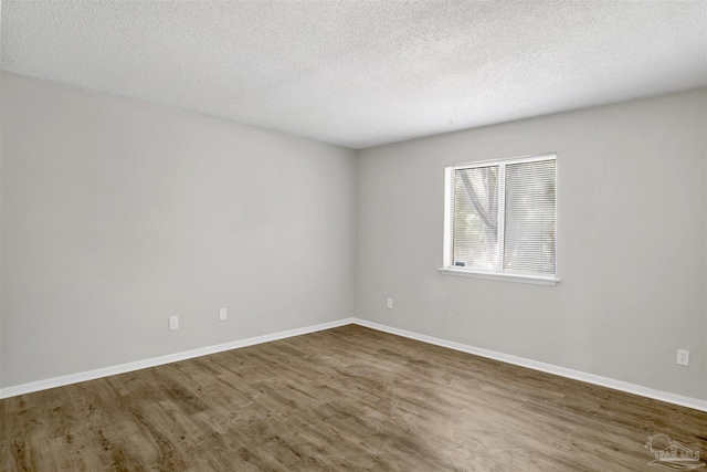 unfurnished room with a textured ceiling, baseboards, and wood finished floors