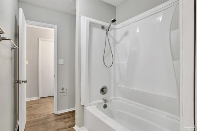 bathroom with tub / shower combination, a textured ceiling, baseboards, and wood finished floors