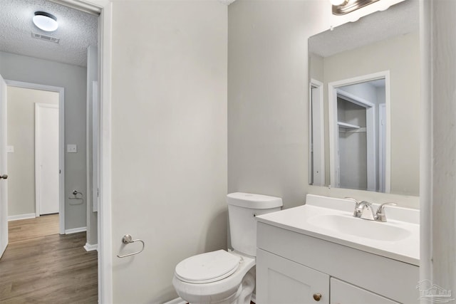 bathroom with a textured ceiling, toilet, wood finished floors, vanity, and visible vents