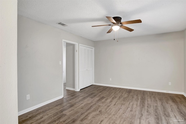 unfurnished room with baseboards, visible vents, a ceiling fan, wood finished floors, and a textured ceiling