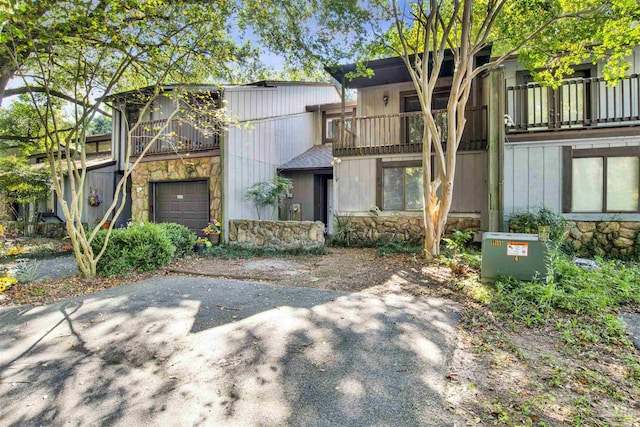 view of front of house featuring driveway, stone siding, and a balcony