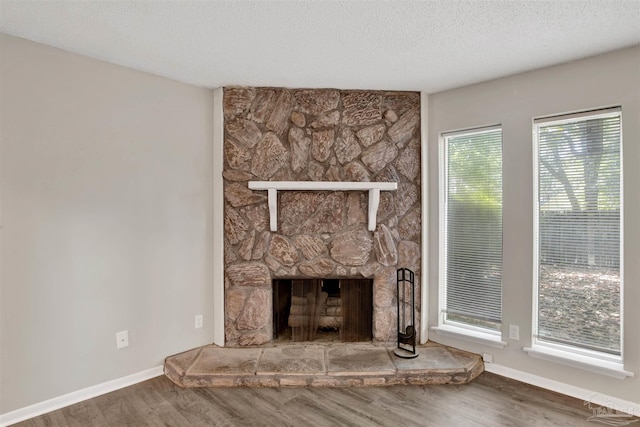 unfurnished living room with a textured ceiling, a stone fireplace, wood finished floors, and baseboards