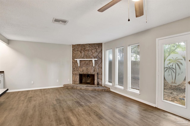 unfurnished living room with visible vents, a stone fireplace, a textured ceiling, wood finished floors, and baseboards