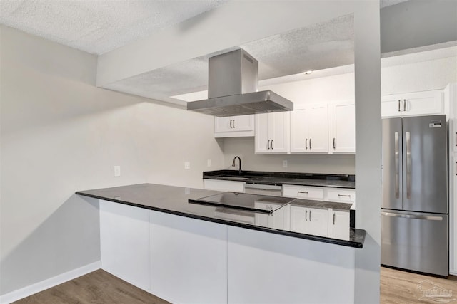 kitchen featuring island range hood, a peninsula, wood finished floors, white cabinets, and freestanding refrigerator