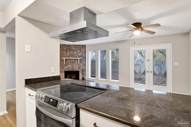 kitchen with island range hood, white cabinetry, french doors, stainless steel electric stove, and dark stone countertops