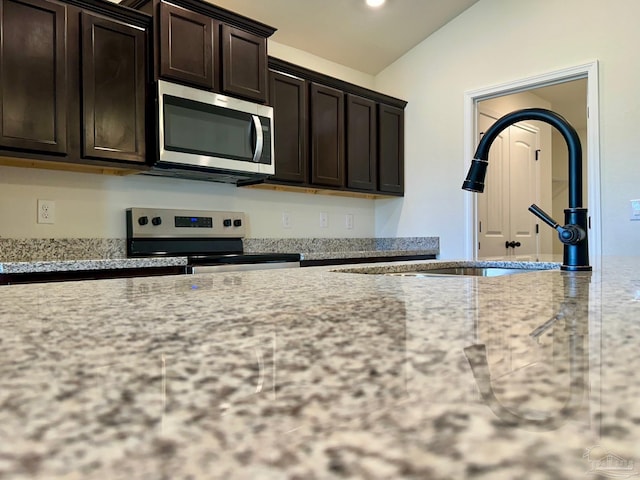 kitchen featuring lofted ceiling, light stone counters, stainless steel appliances, dark brown cabinetry, and sink