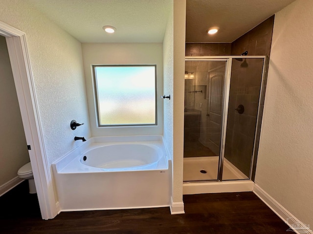 bathroom with plus walk in shower, toilet, a textured ceiling, and hardwood / wood-style flooring