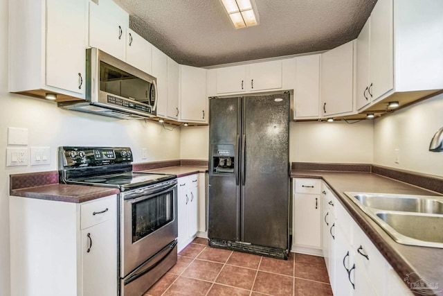 kitchen with sink, white cabinetry, stainless steel appliances, a textured ceiling, and dark tile patterned flooring